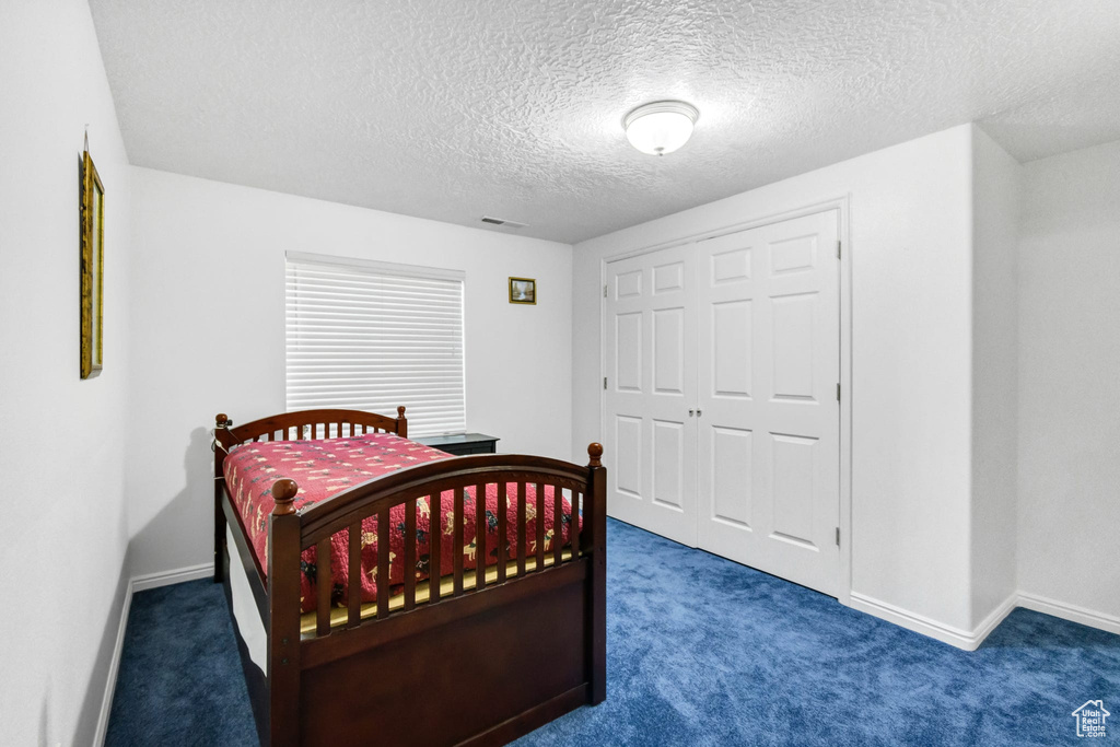 Bedroom with carpet, baseboards, a textured ceiling, and a closet