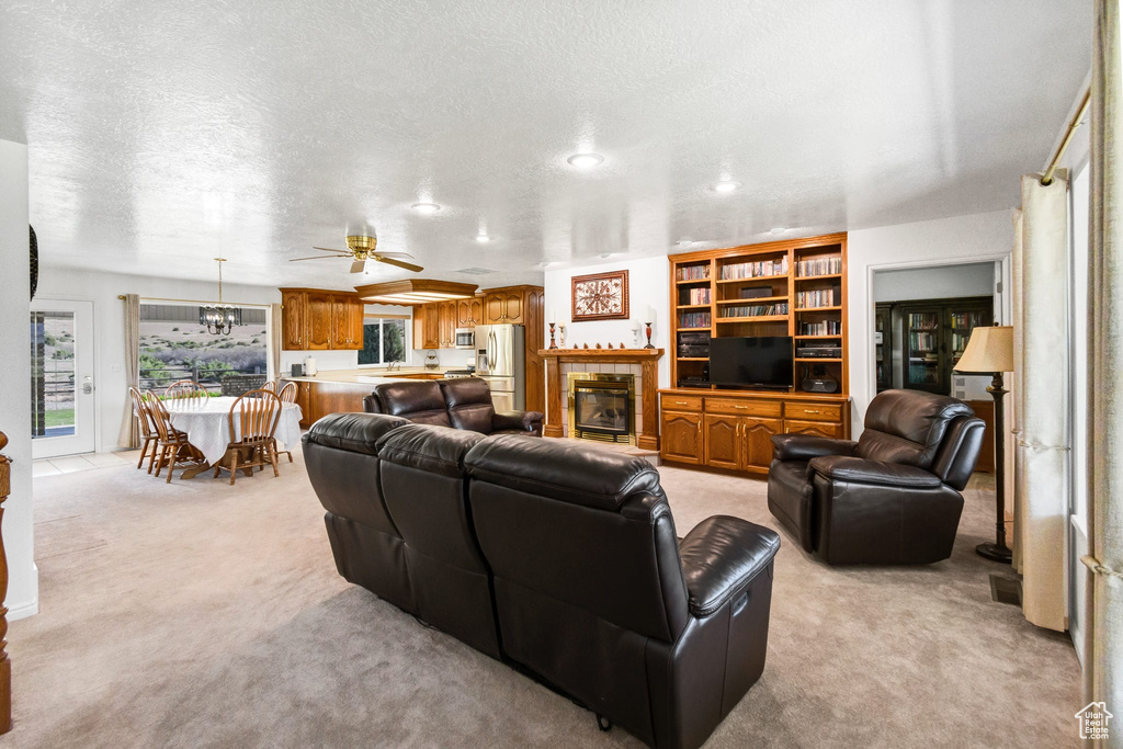 Living room featuring light colored carpet, ceiling fan, a tile fireplace, and a textured ceiling