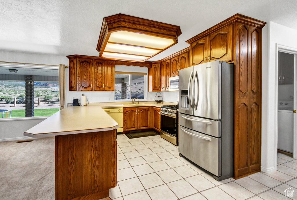 Kitchen with stainless steel appliances, a peninsula, a sink, light countertops, and brown cabinets
