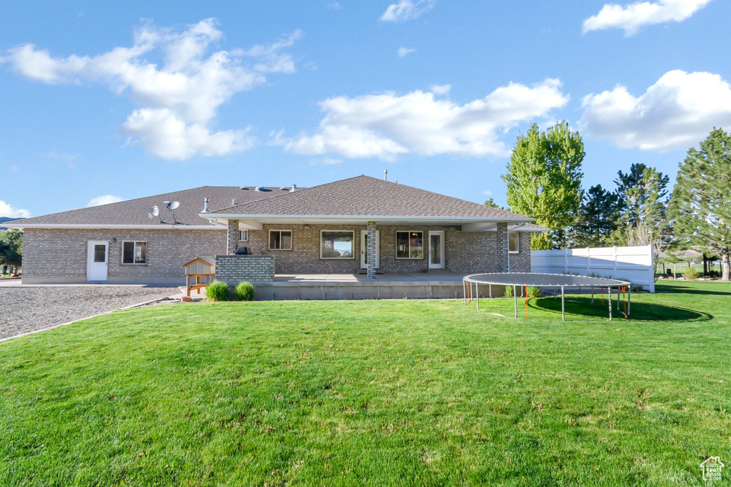 Back of property with a trampoline, brick siding, a lawn, and a shingled roof