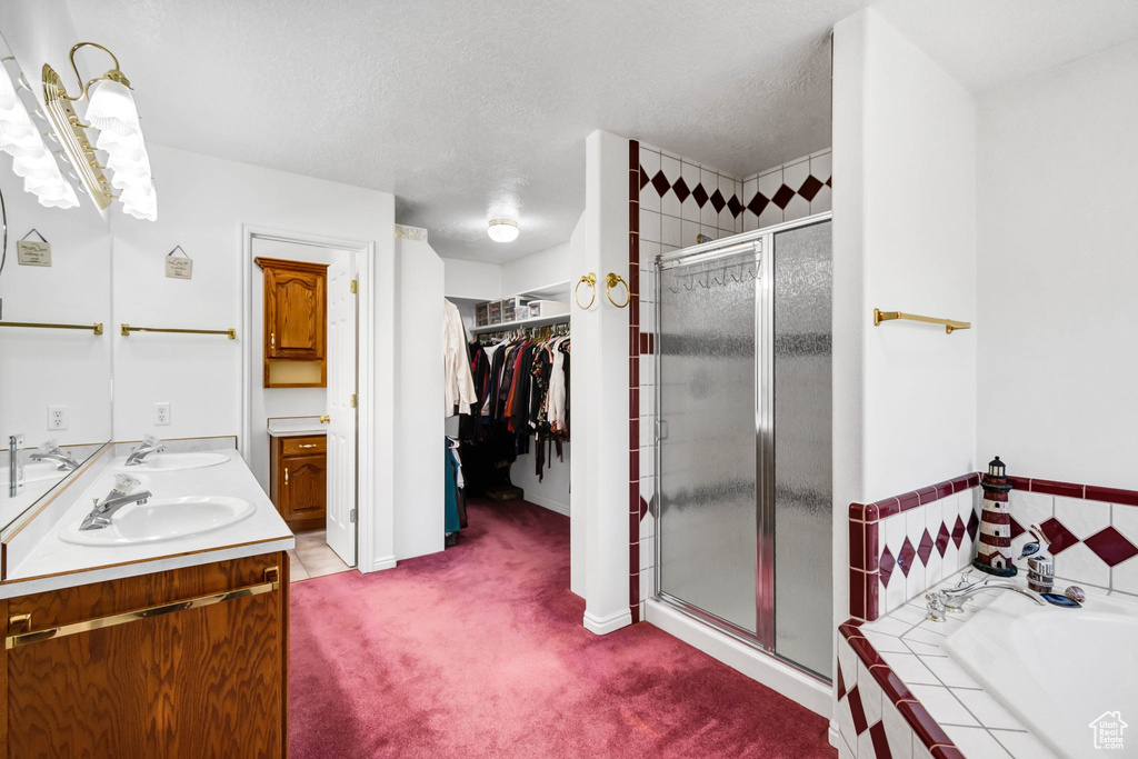 Bathroom featuring a shower stall, a garden tub, a walk in closet, double vanity, and a textured ceiling