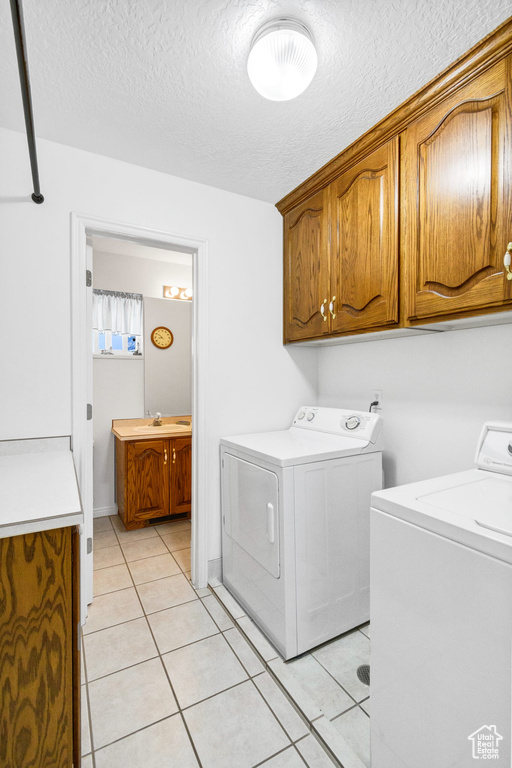 Laundry room with independent washer and dryer, cabinet space, light tile patterned floors, and a textured ceiling