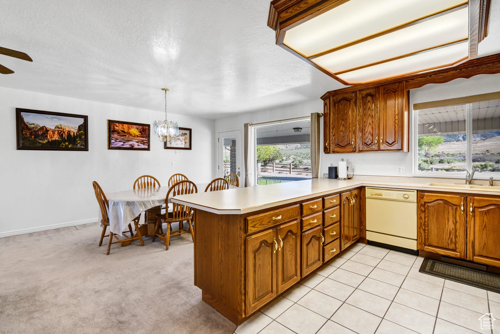Kitchen featuring white dishwasher, a sink, a peninsula, light countertops, and brown cabinets
