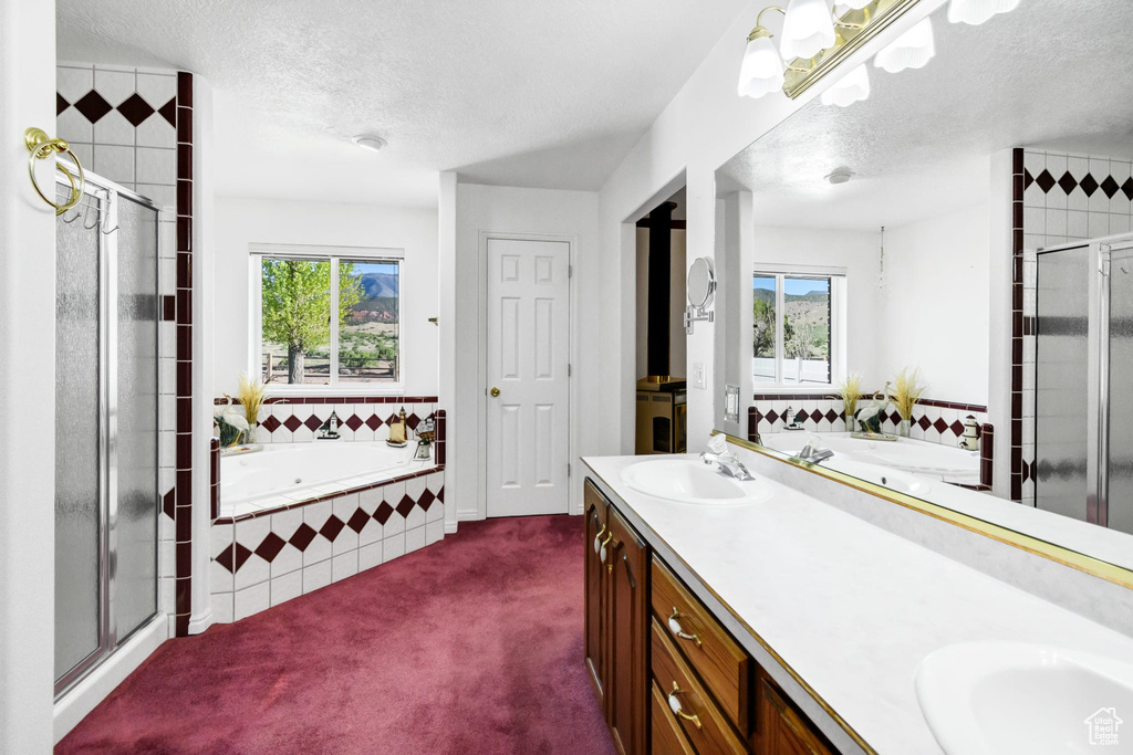 Bathroom featuring healthy amount of natural light, a textured ceiling, a stall shower, a garden tub, and double vanity