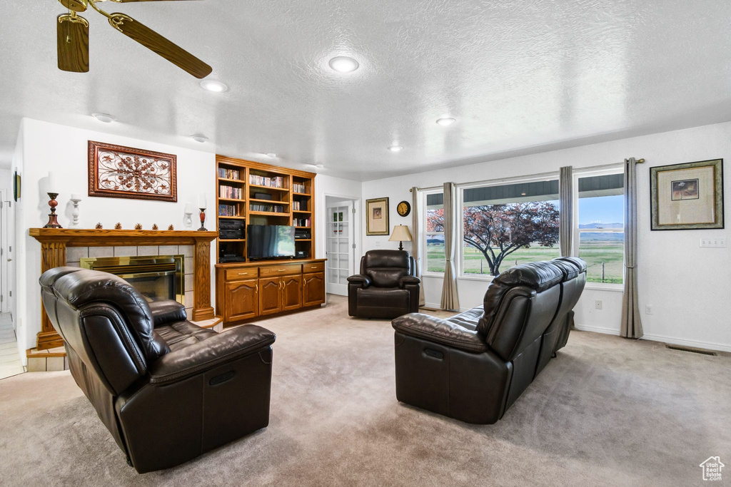 Living room featuring light colored carpet, ceiling fan, a textured ceiling, a fireplace, and recessed lighting