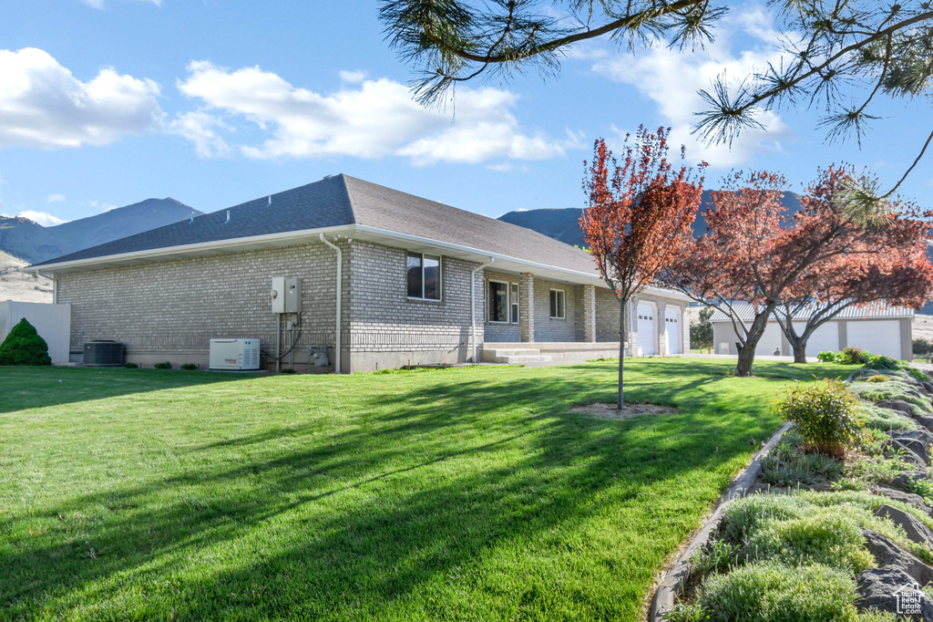 Back of house with central air condition unit, brick siding, a garage, a yard, and a shingled roof