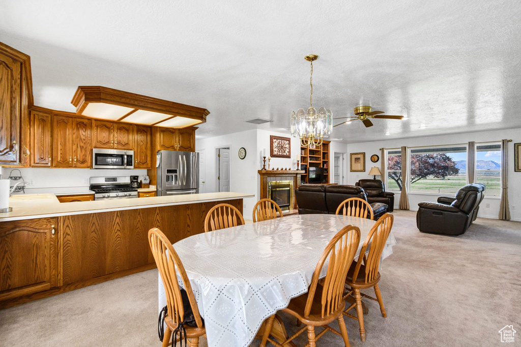Dining area with light carpet, a chandelier, a glass covered fireplace, and a ceiling fan