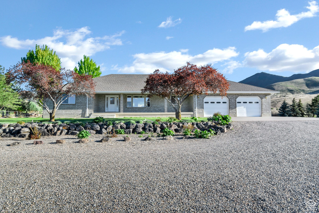 Ranch-style home with brick siding, gravel driveway, an attached garage, a mountain view, and a shingled roof