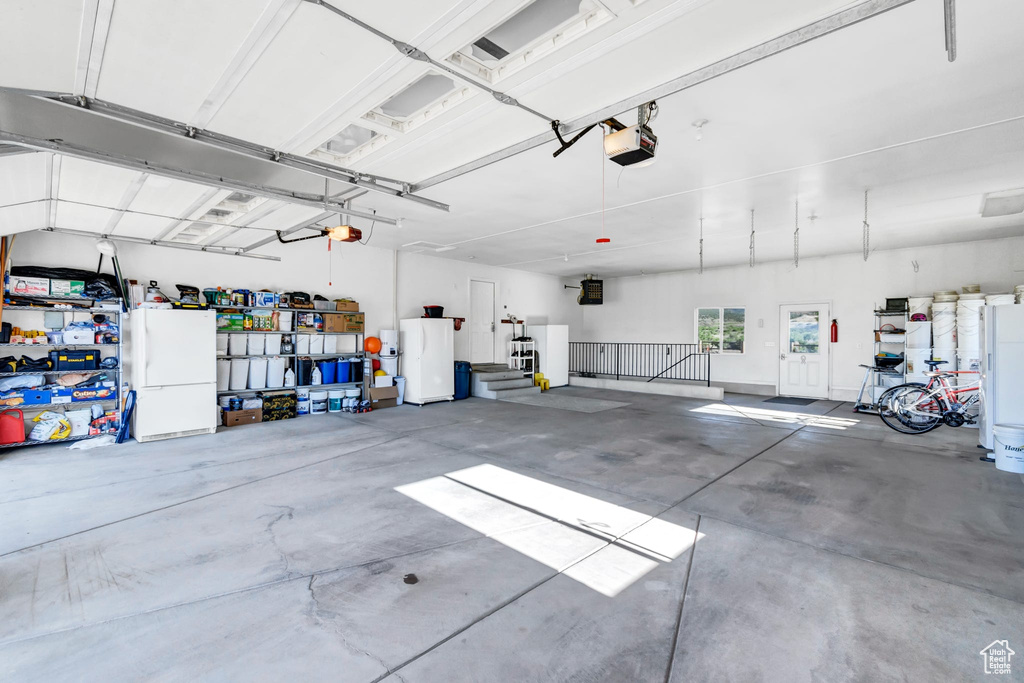 Garage featuring a garage door opener, freestanding refrigerator, and refrigerator