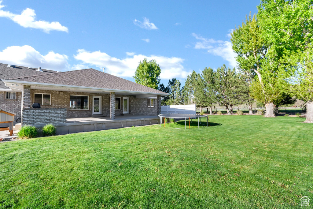 Back of property featuring a trampoline, brick siding, a yard, a shingled roof, and a patio