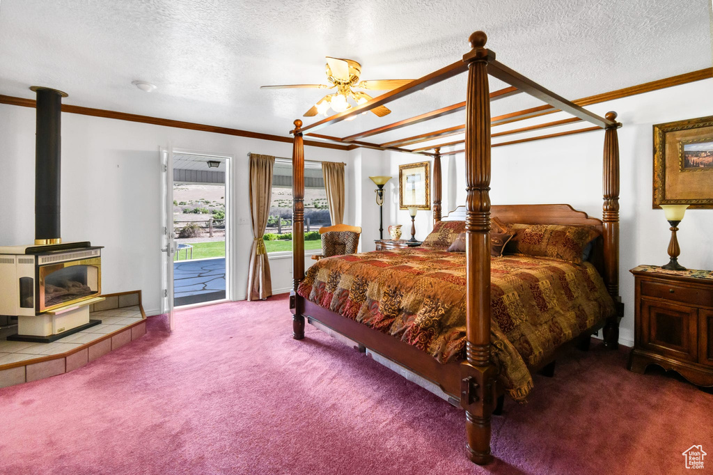 Bedroom featuring a wood stove, access to outside, carpet floors, crown molding, and a textured ceiling