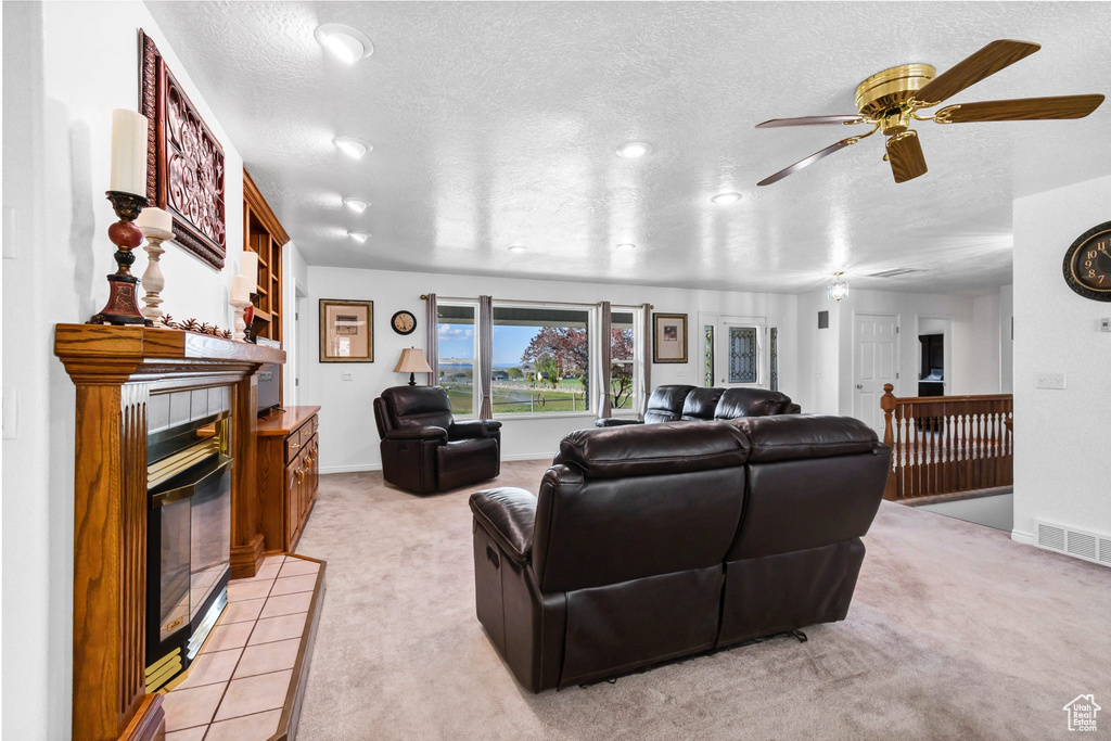 Living room with a tile fireplace, a textured ceiling, light colored carpet, ceiling fan, and baseboards