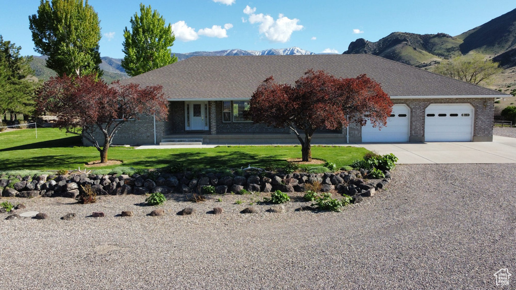 View of front of home featuring a mountain view, brick siding, driveway, an attached garage, and a front yard