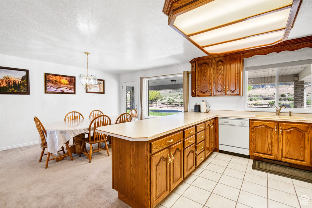 Kitchen featuring white dishwasher, a sink, brown cabinets, a peninsula, and light countertops