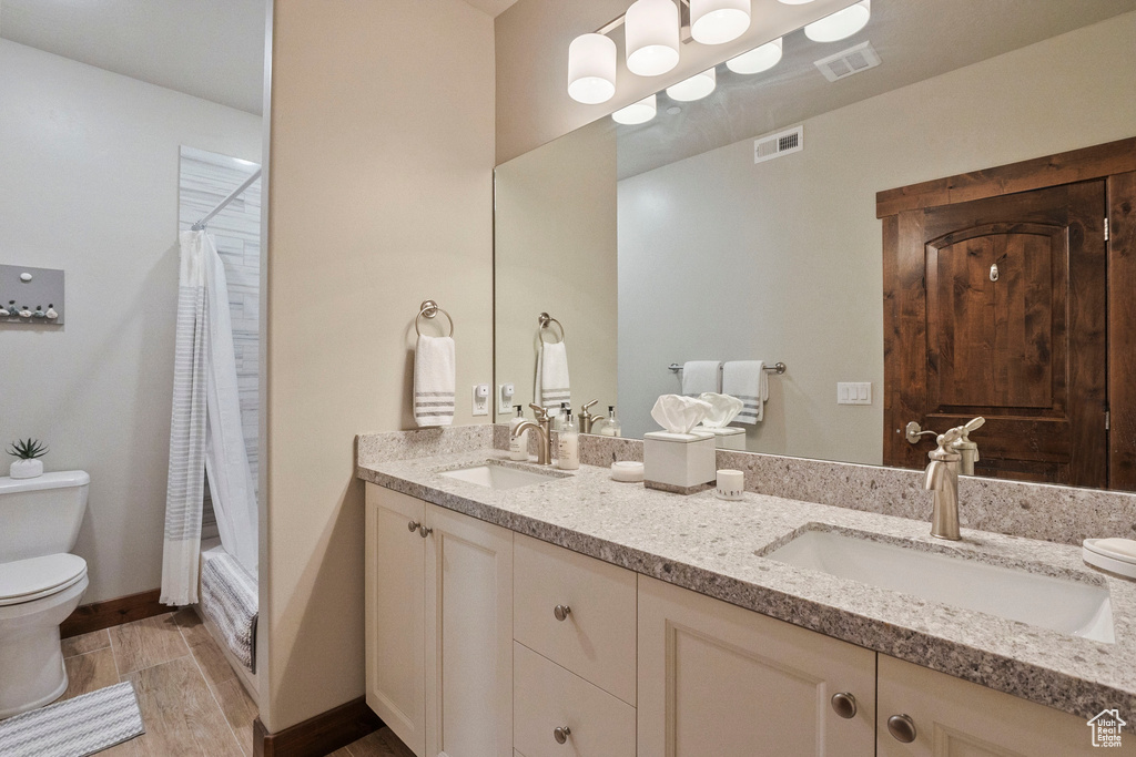 Bathroom featuring toilet, double vanity, shower / tub combo, and wood finished floors