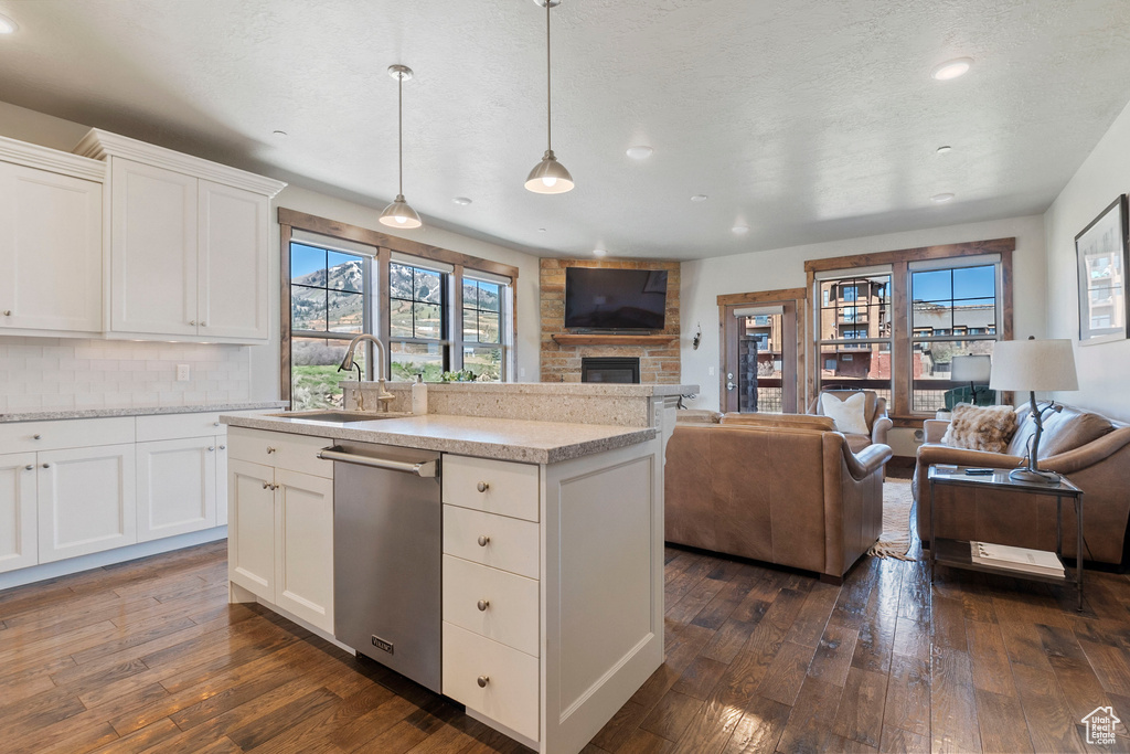 Kitchen featuring a sink, stainless steel dishwasher, open floor plan, a fireplace, and dark wood-type flooring