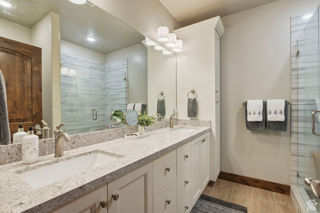 Full bathroom with a shower stall, double vanity, wood finished floors, and baseboards
