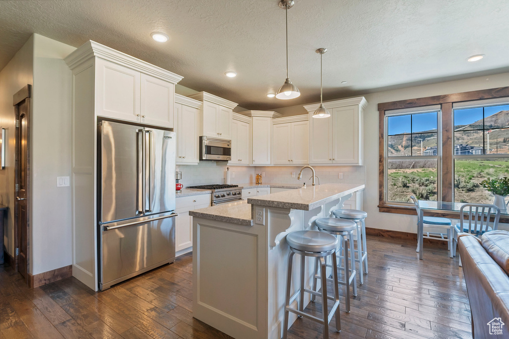 Kitchen featuring high quality appliances, baseboards, dark wood-style floors, white cabinetry, and a breakfast bar area