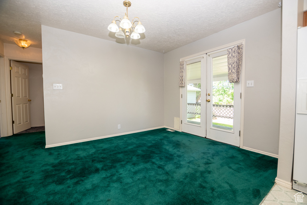 Carpeted spare room featuring french doors, a textured ceiling, and a chandelier