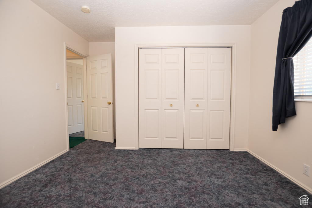 Unfurnished bedroom featuring dark carpet and a closet