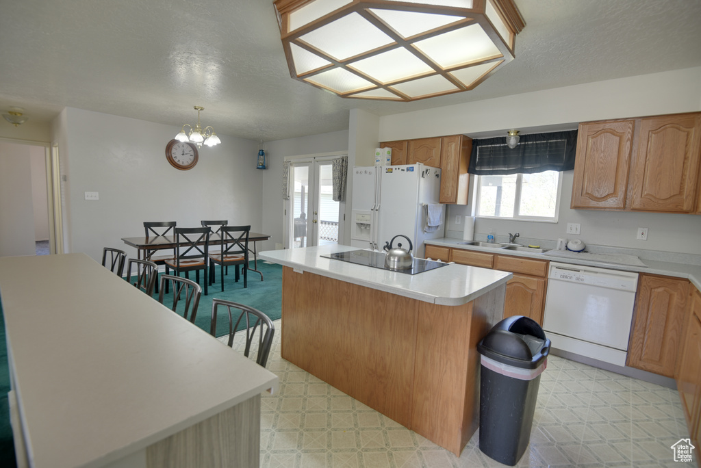 Kitchen featuring white appliances, a sink, light floors, a center island, and light countertops