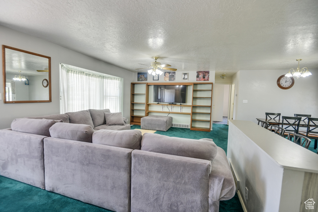 Carpeted living room featuring a textured ceiling, a chandelier, and ceiling fan
