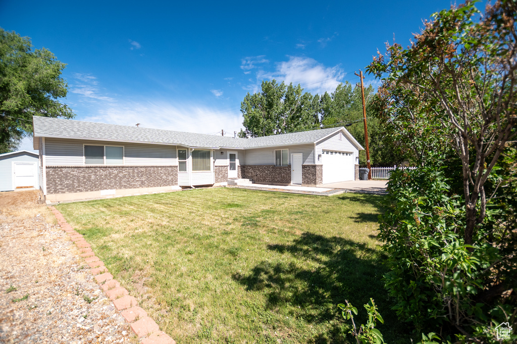 Single story home with brick siding, a shed, a garage, driveway, and roof with shingles