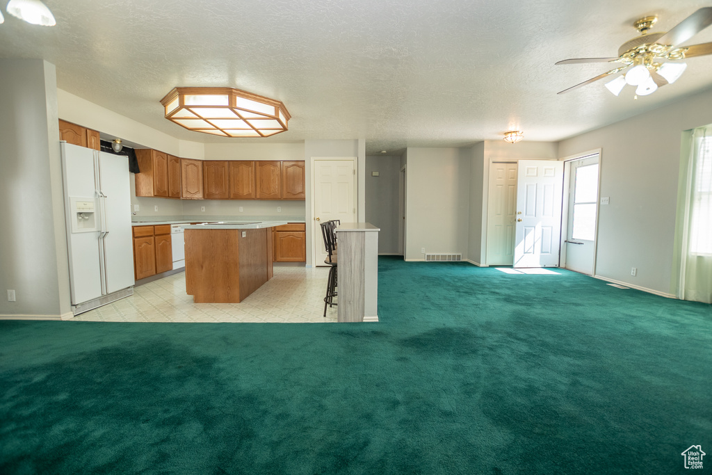 Kitchen featuring white appliances, a center island, light countertops, brown cabinetry, and a ceiling fan