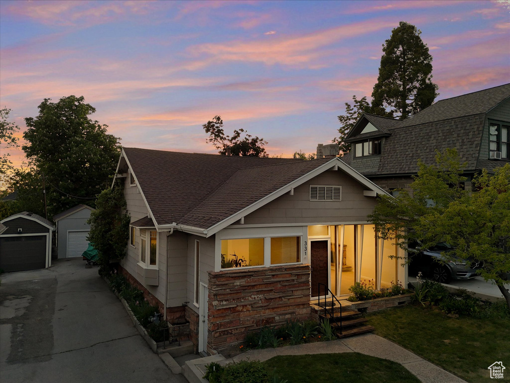View of front facade featuring concrete driveway, an outbuilding, roof with shingles, and a garage