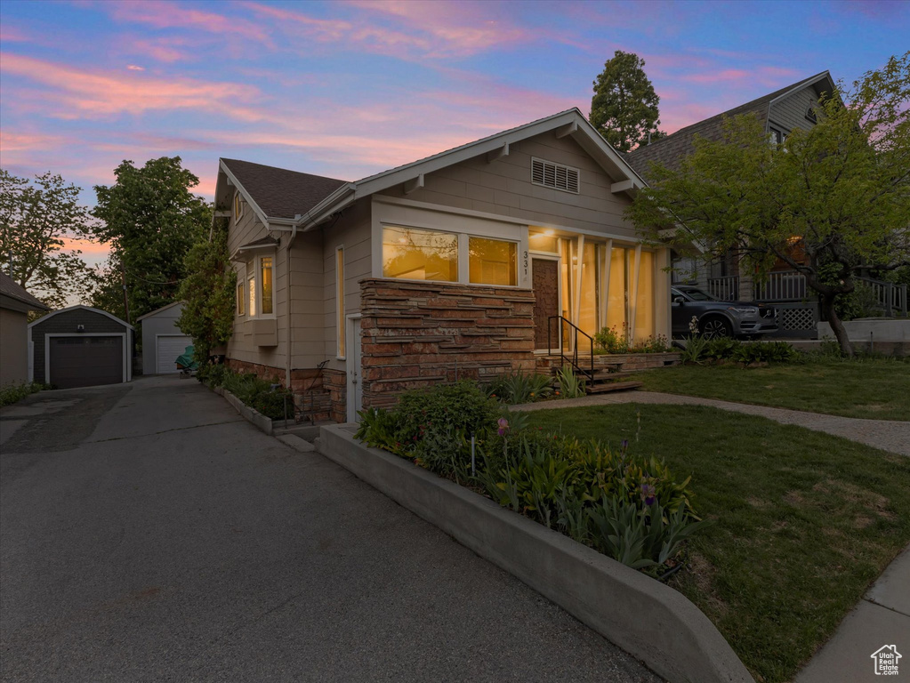 Bungalow-style home with stone siding, a garage, an outbuilding, and a lawn