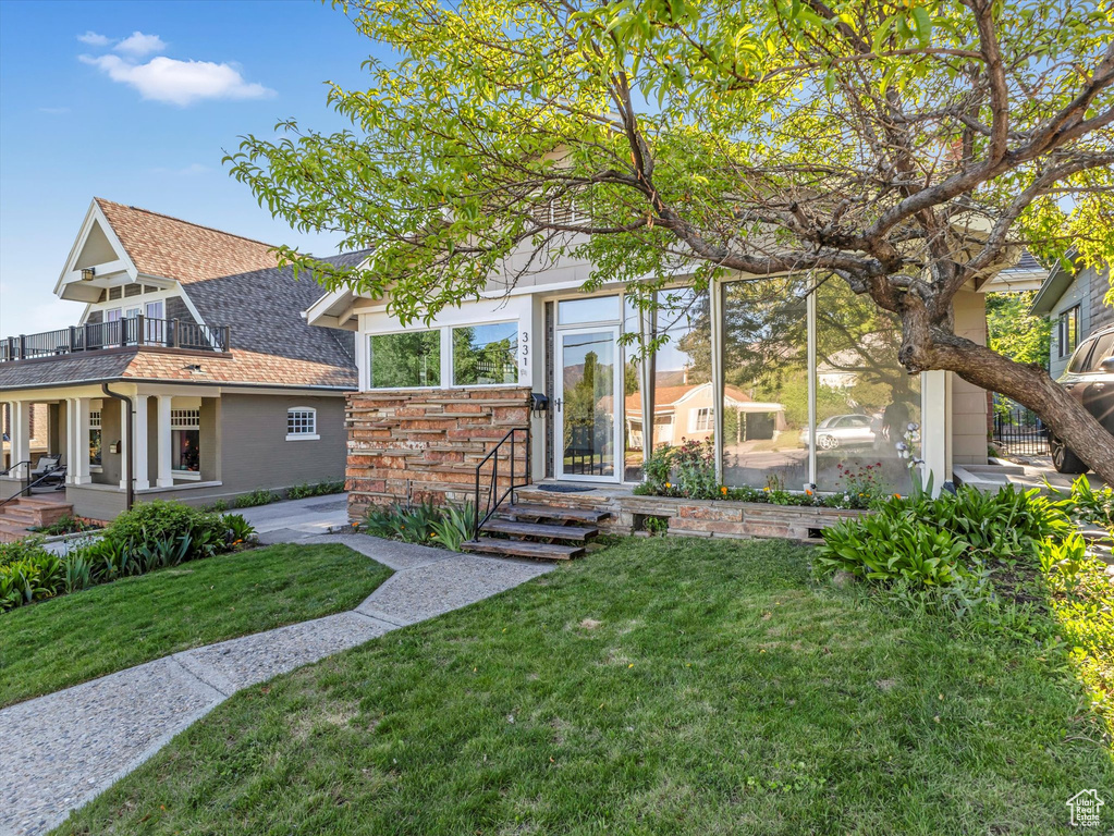 View of front of home featuring a balcony, a front yard, and roof with shingles