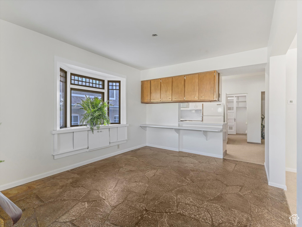 Kitchen featuring freestanding refrigerator, stone finish flooring, light countertops, brown cabinets, and a breakfast bar