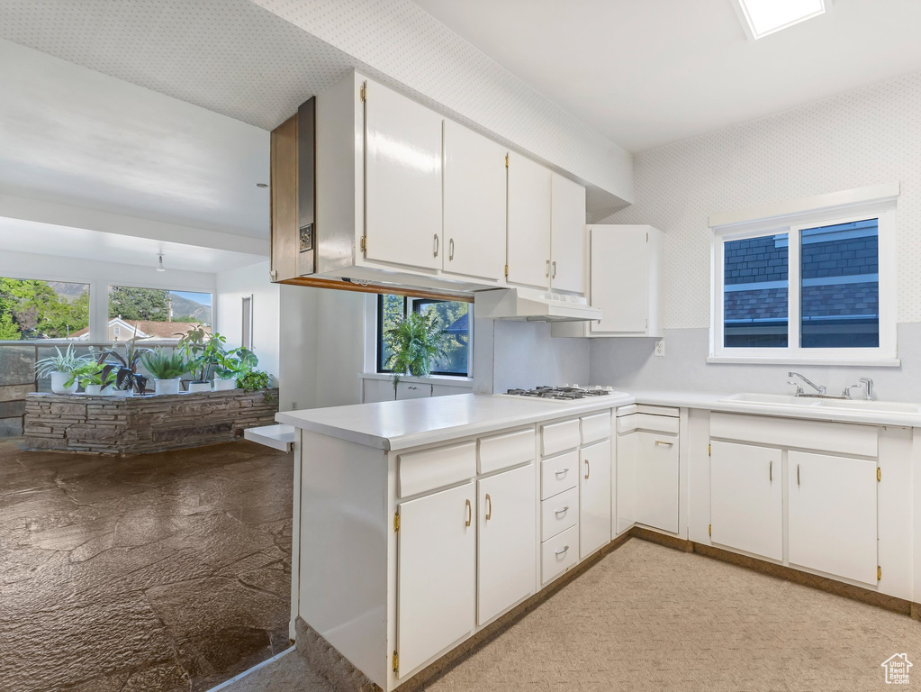 Kitchen featuring a sink, under cabinet range hood, white cabinetry, and light countertops