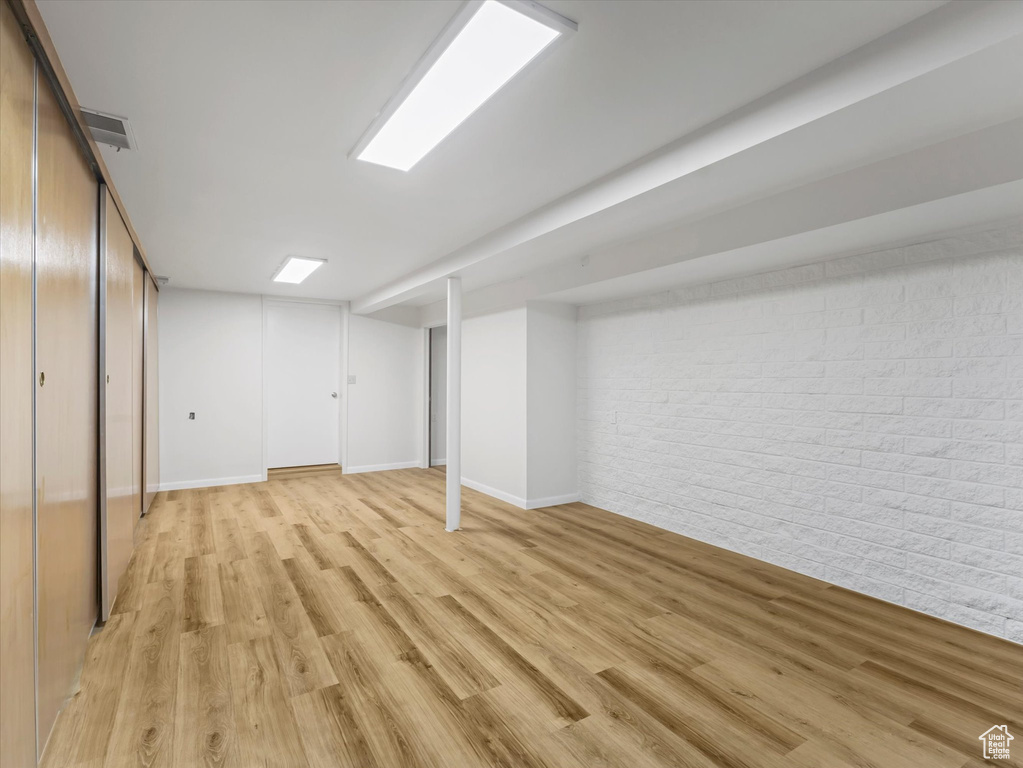 Finished below grade area with brick wall, light wood-type flooring, and baseboards