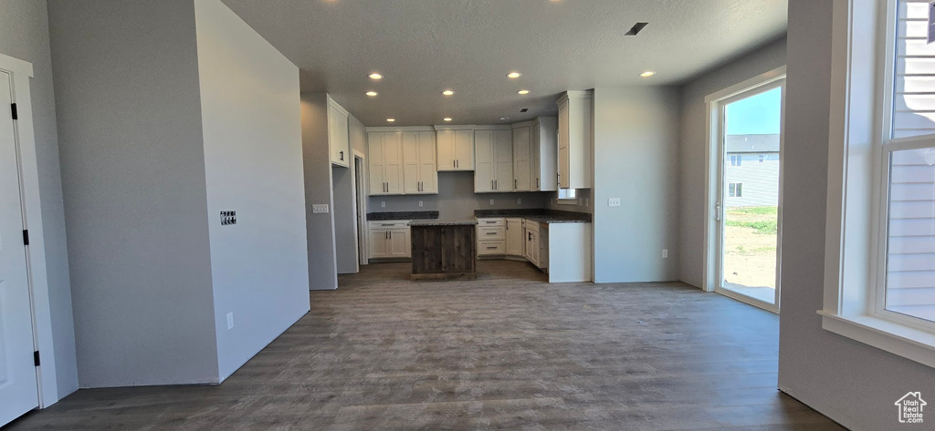 Kitchen with dark wood-style floors, recessed lighting, dark countertops, white cabinets, and open floor plan