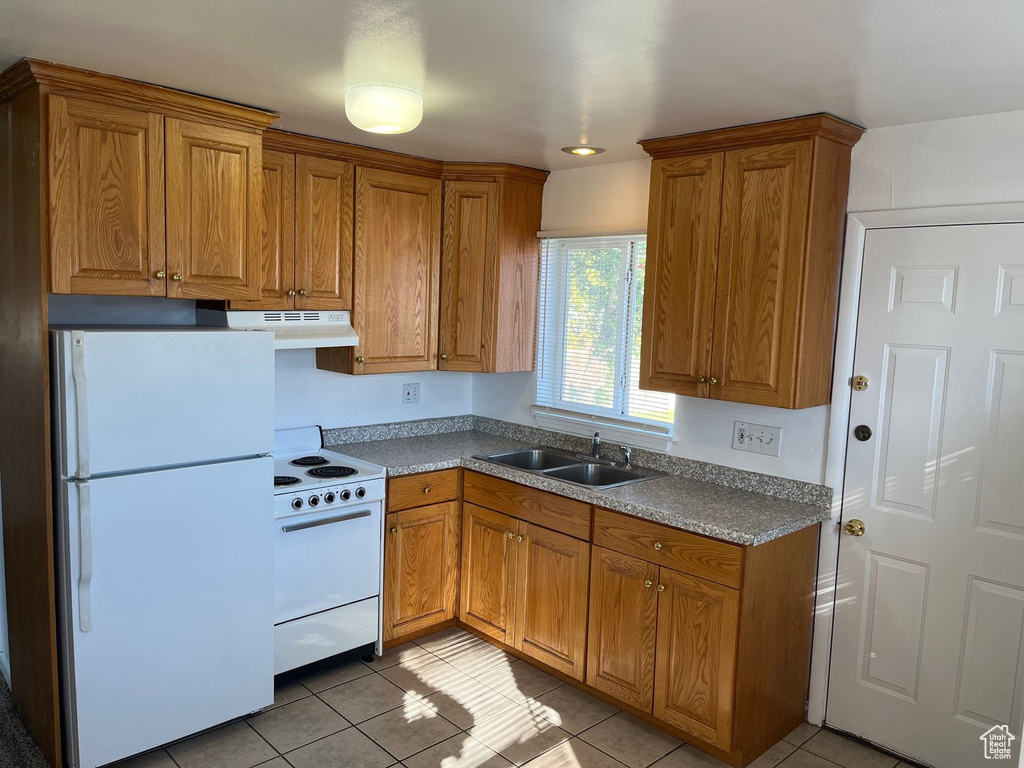 Kitchen featuring white appliances, a sink, under cabinet range hood, and brown cabinetry