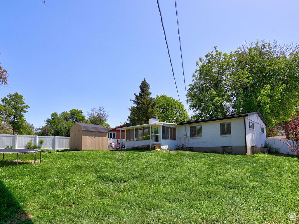 Back of property featuring a storage unit, a sunroom, an outbuilding, a trampoline, and brick siding