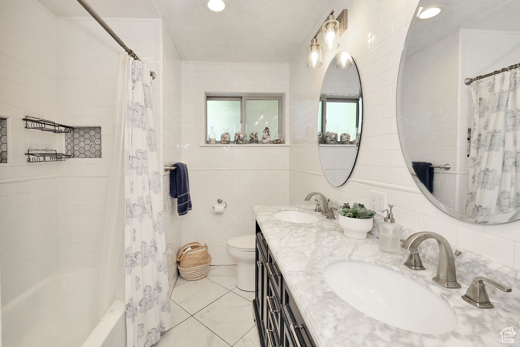 Bathroom featuring tile walls, toilet, shower / tub combo, and double vanity
