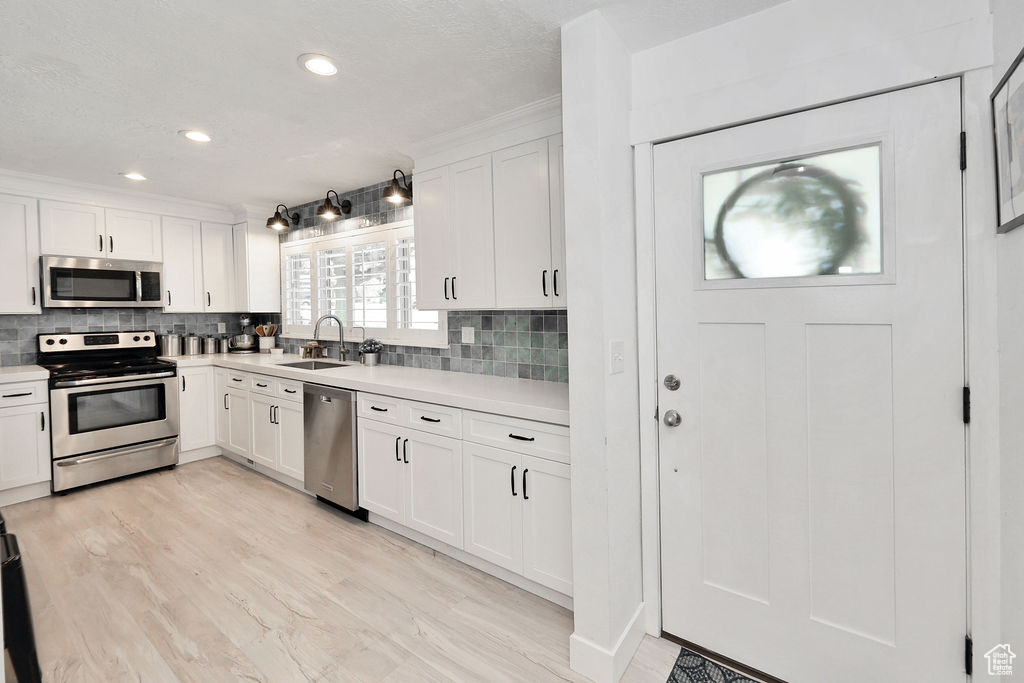 Kitchen with stainless steel appliances, a sink, light countertops, decorative backsplash, and recessed lighting
