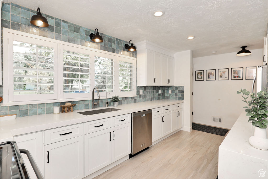 Kitchen featuring dishwasher, a sink, backsplash, white cabinetry, and light wood-style flooring