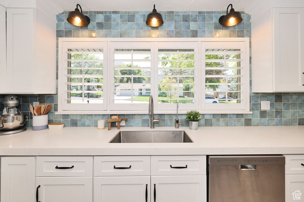 Kitchen featuring stainless steel dishwasher, a sink, tasteful backsplash, and light countertops