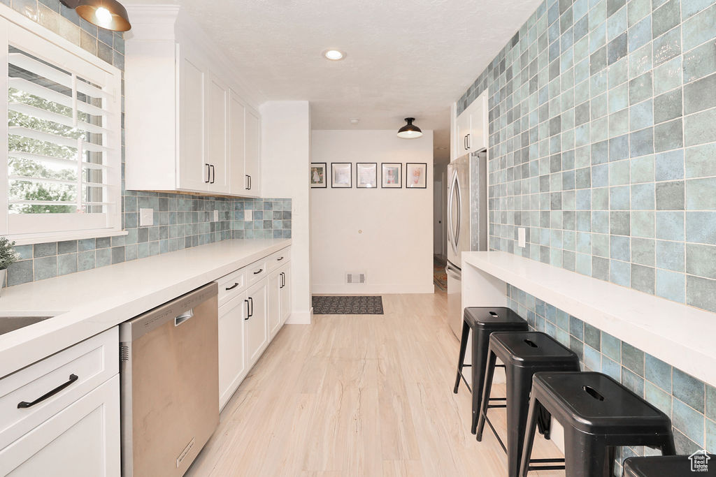 Kitchen with stainless steel appliances, white cabinets, light countertops, light wood finished floors, and tile walls
