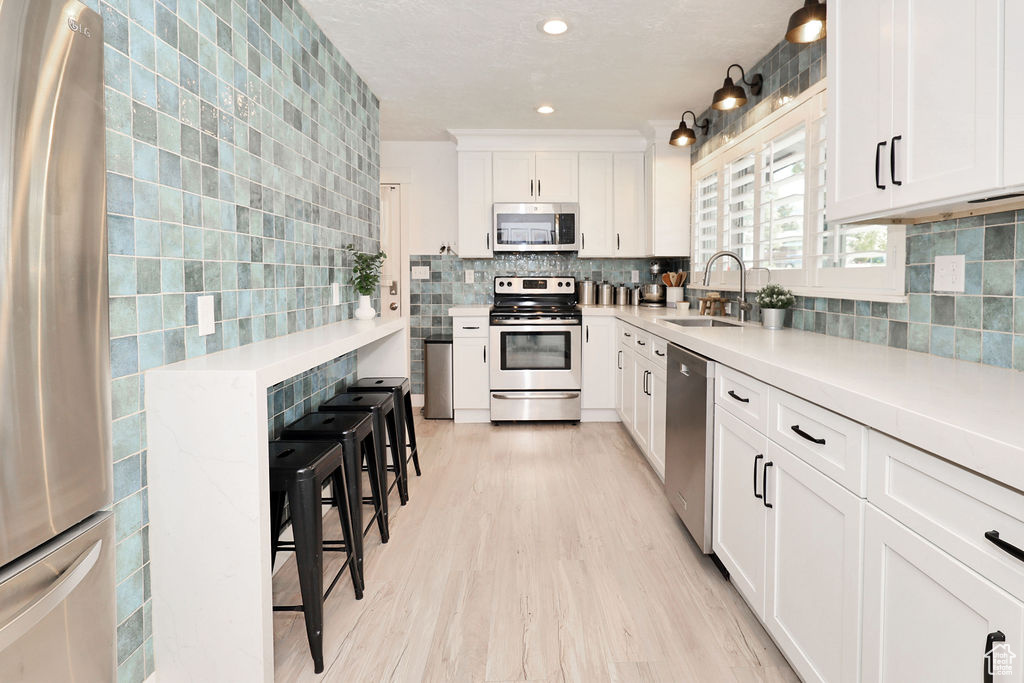 Kitchen with appliances with stainless steel finishes, a sink, backsplash, light wood-style floors, and white cabinets