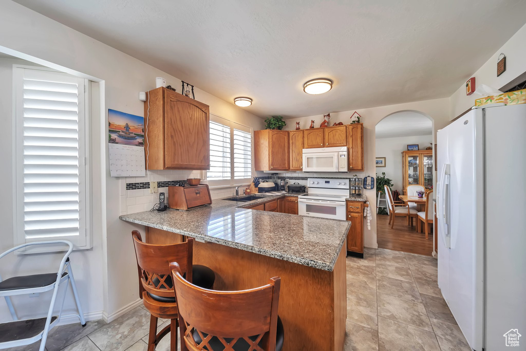 Kitchen with white appliances, a peninsula, arched walkways, a sink, and tasteful backsplash
