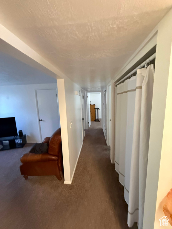 Corridor featuring carpet flooring, baseboards, and a textured ceiling