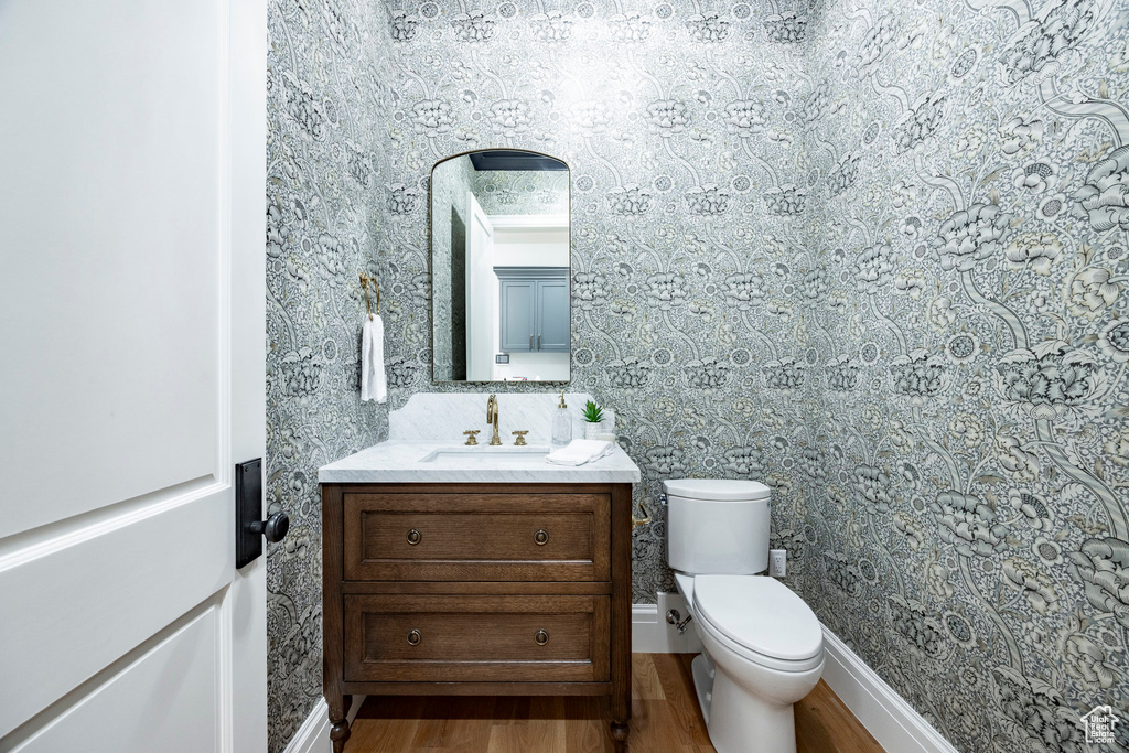 Bathroom with wood finished floors, wallpapered walls, vanity, toilet, and baseboards