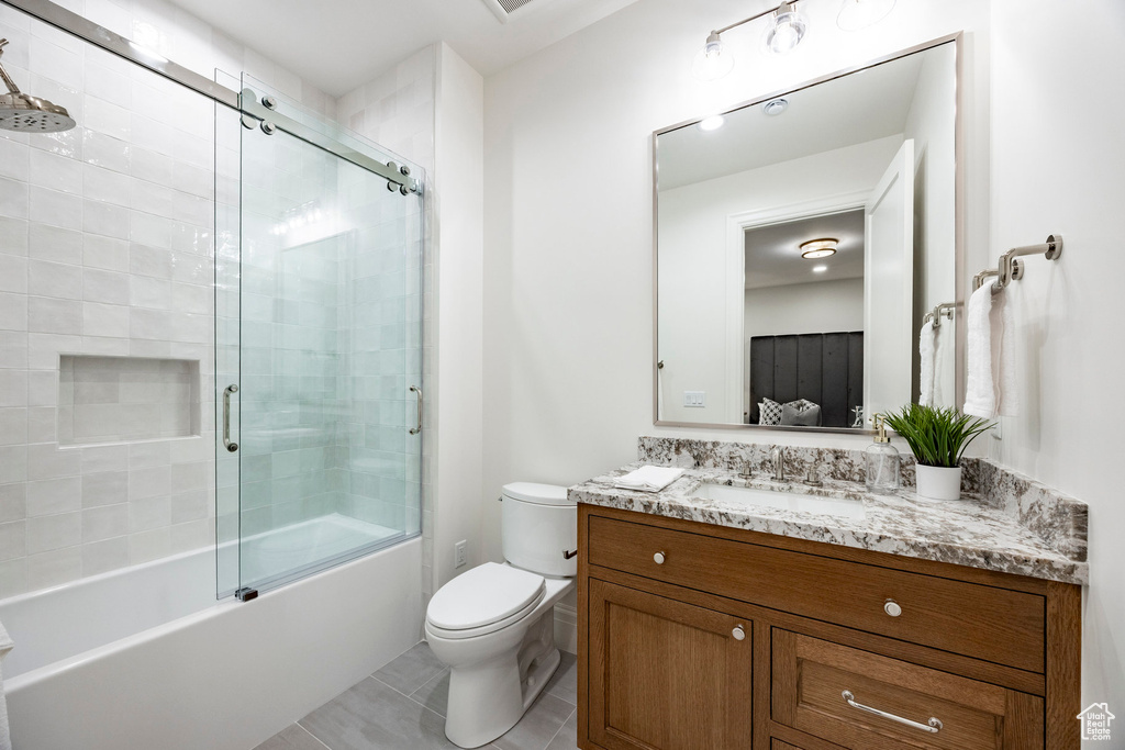 Bathroom with toilet, tile patterned floors, vanity, and bath / shower combo with glass door