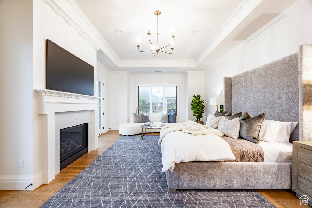 Bedroom featuring a chandelier, a raised ceiling, a glass covered fireplace, wood finished floors, and ornamental molding