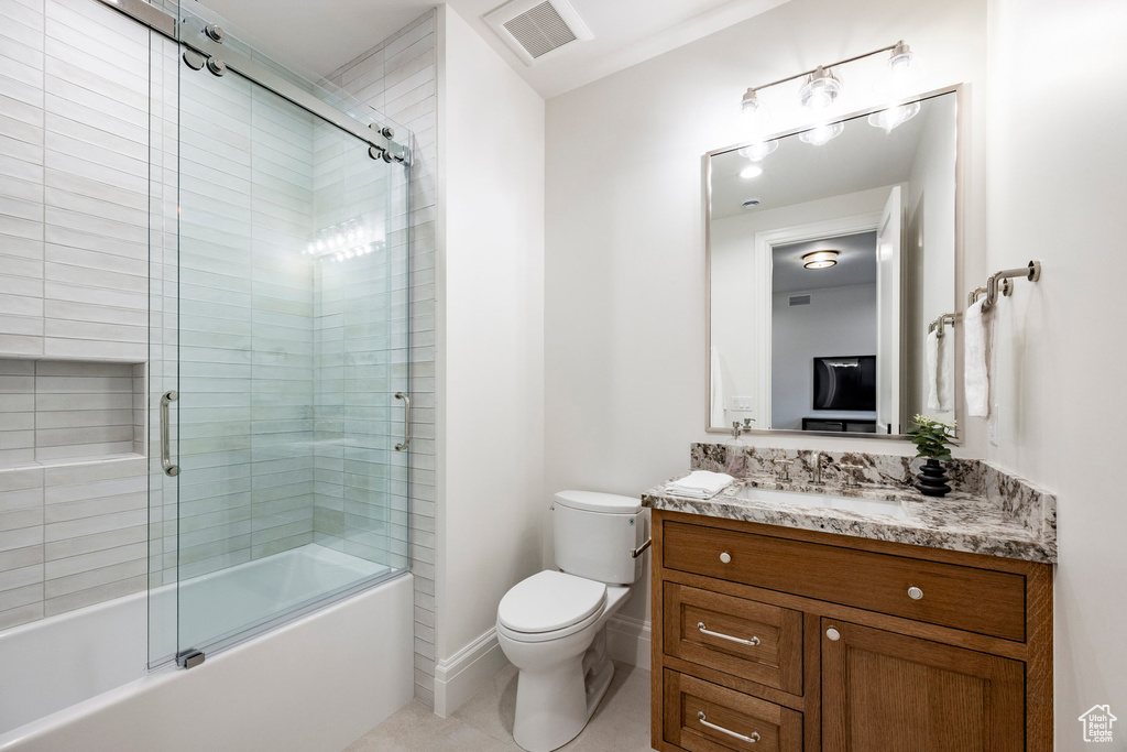 Bathroom featuring toilet, vanity, bath / shower combo with glass door, and tile patterned flooring
