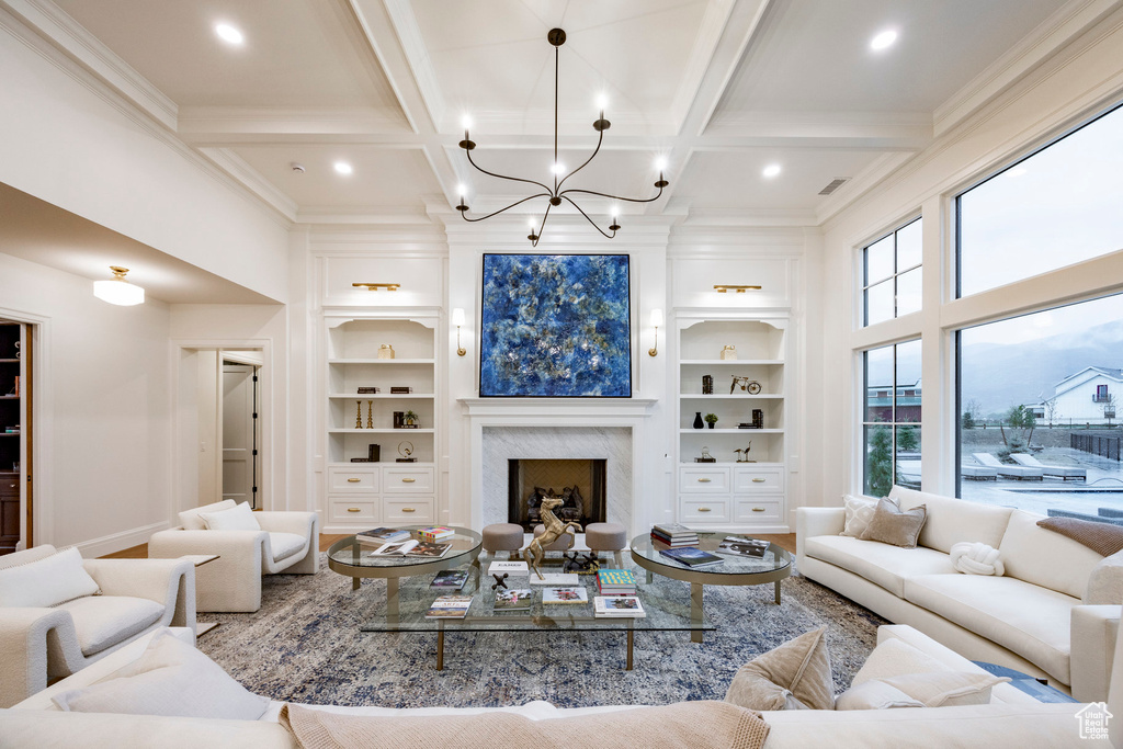 Living room with coffered ceiling, built in shelves, crown molding, beam ceiling, and a chandelier
